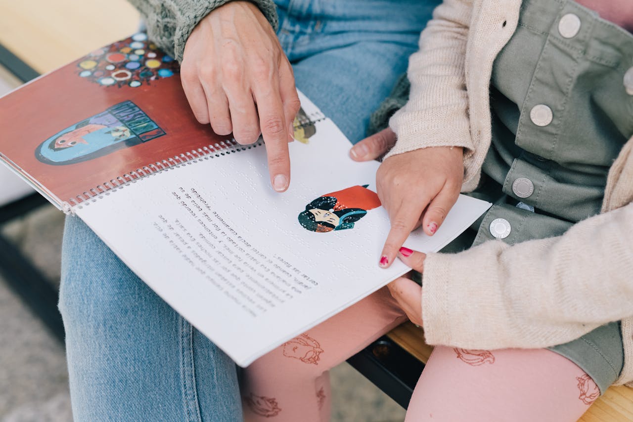 A mother and child enjoy reading a Braille storybook together outdoors, fostering bonding and learning.